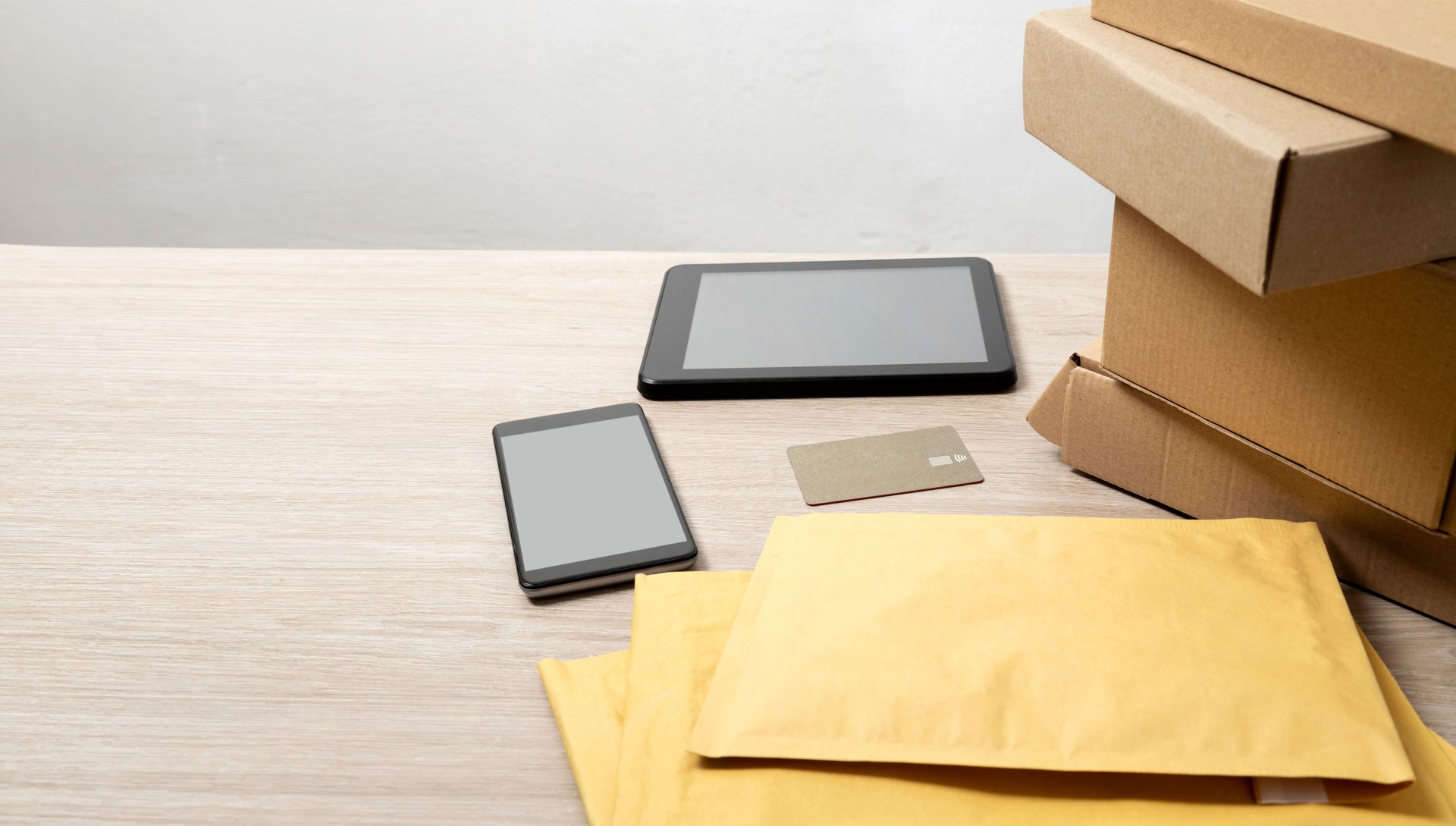 Delivery office.Boxes,padded mailers,credit card,smartphone and pc tablet with blank screen on the desk.Empty space